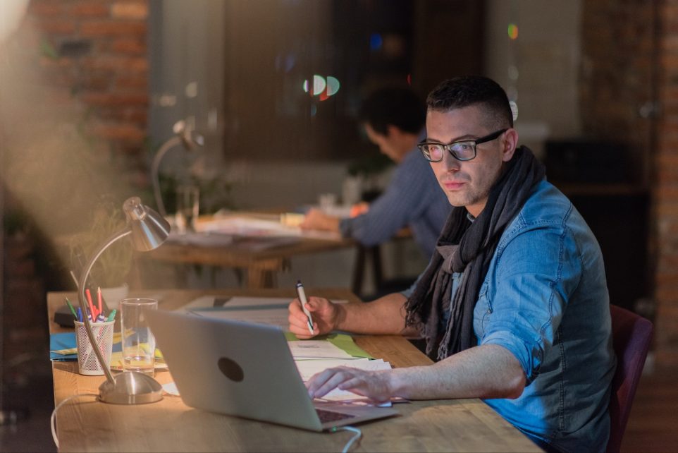 Young man using laptop while working in office at night.