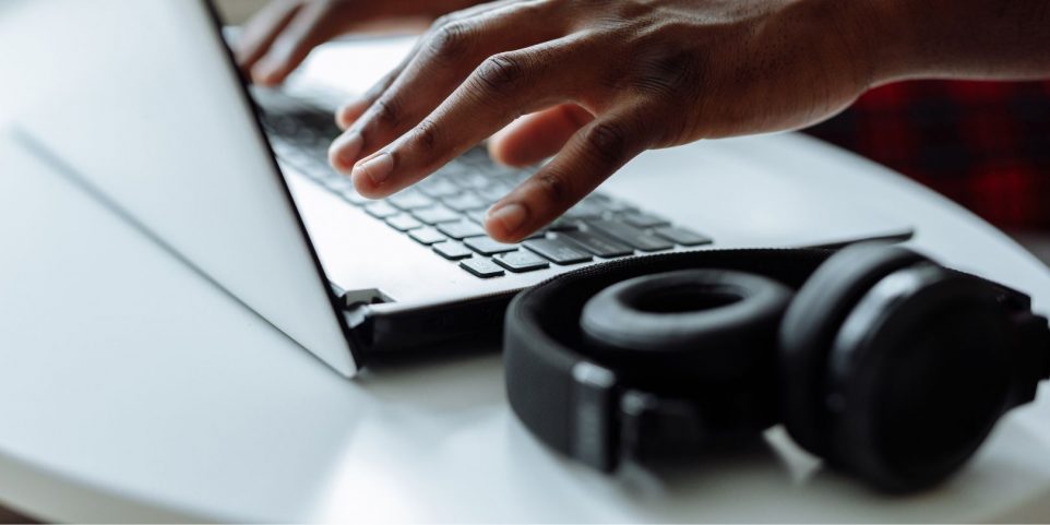 Close-Up Photograph of a Person's Hands Typing on a Laptop Beside Headphones